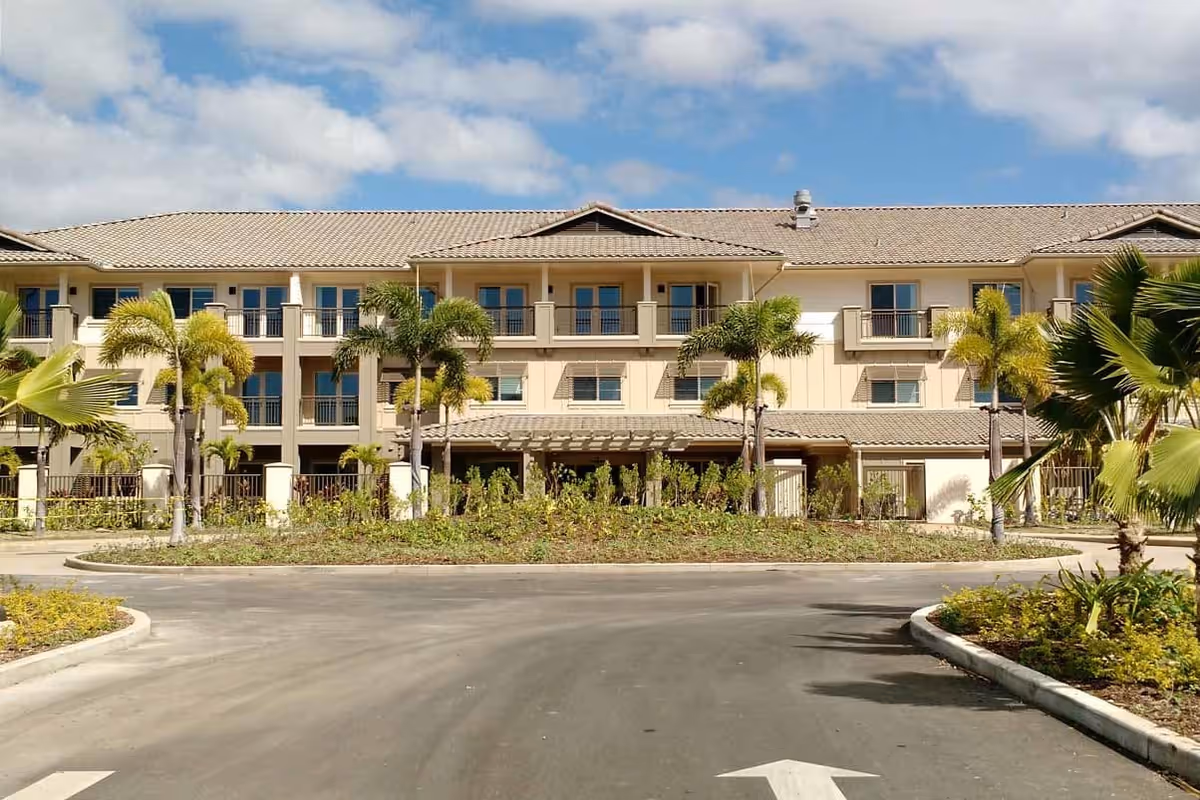 Two-story beige senior living building with balconies and palm trees along a curved driveway.
