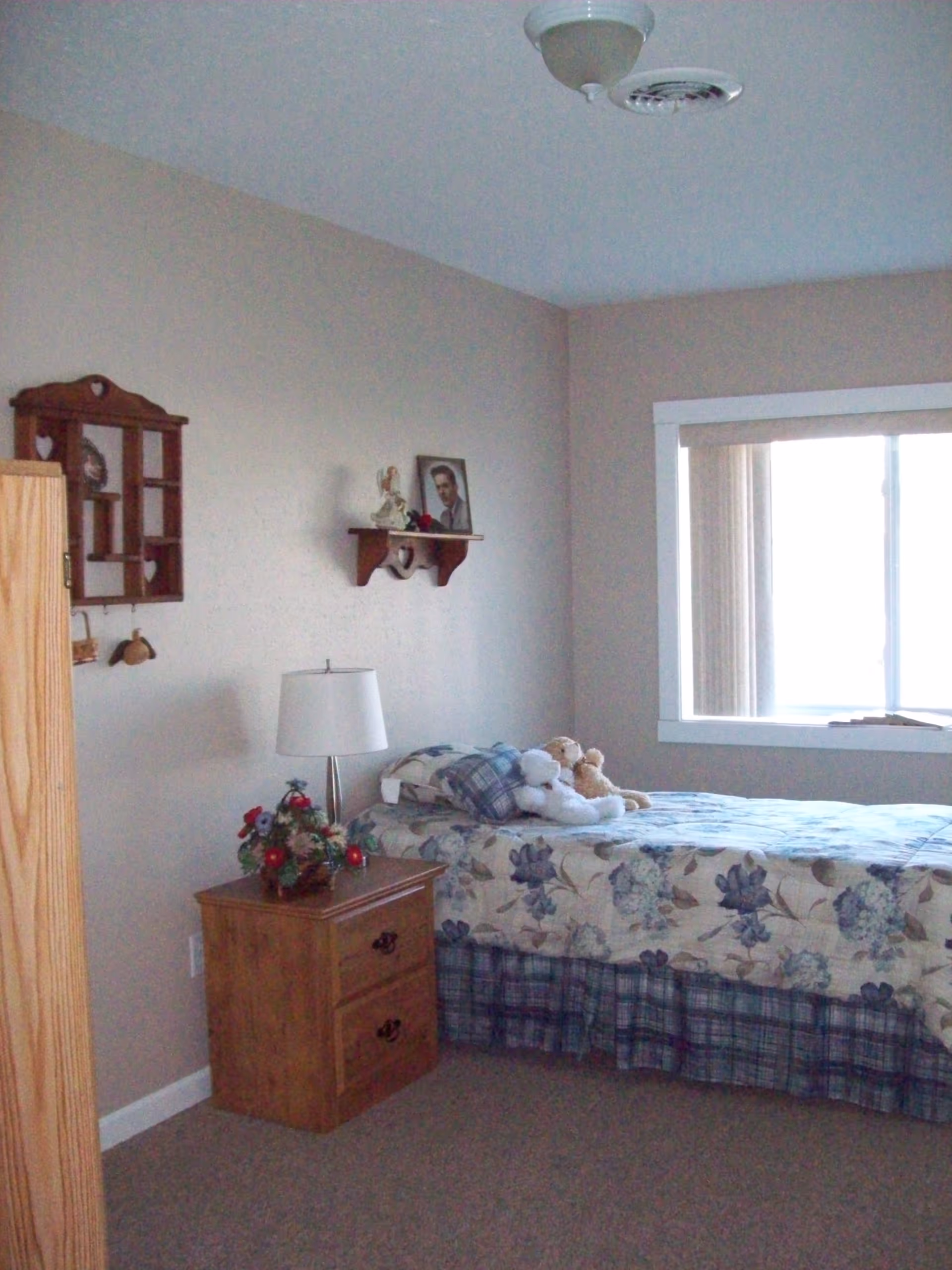 Simple bedroom with a single bed, nightstand and lamp, wall shelves, and a window.