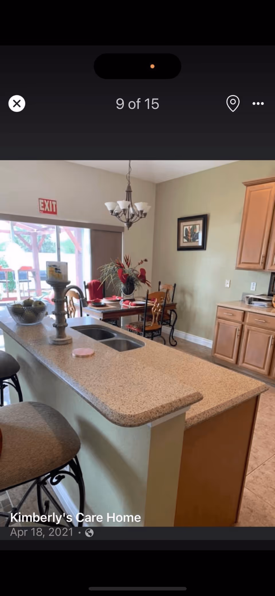Bright kitchen with a long countertop island and sink, bar stools, and a dining table visible in the background.