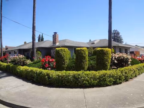 Single-story senior living facility with a circular driveway and manicured hedges.