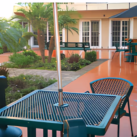 Patio seating area with green tables and chairs under umbrellas overlooking a landscaped courtyard and building windows.