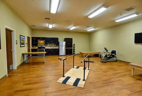 Indoor senior living facility space featuring kitchenette, exercise equipment, and benches.