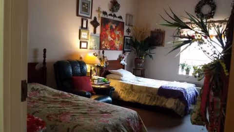 Two beds in a senior living bedroom with wall art, plants, and a lamp.