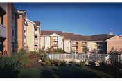 Exterior view of a multi-story senior living facility building with balconies, surrounded by landscaped greenery and a clear blue sky.