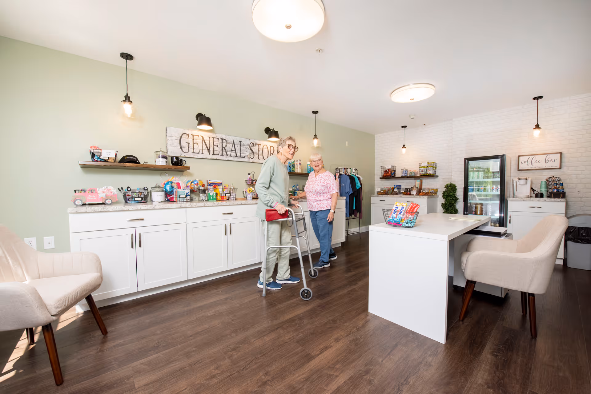 Two elderly women standing in a bright 'General Store' area of a senior living facility with shelves, a counter, and seating.