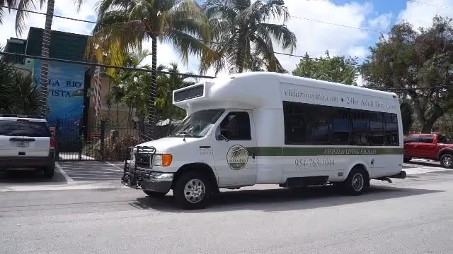 A white Villa Rio Vista shuttle bus parked on the street in front of the facility with palm trees and the building entrance visible.