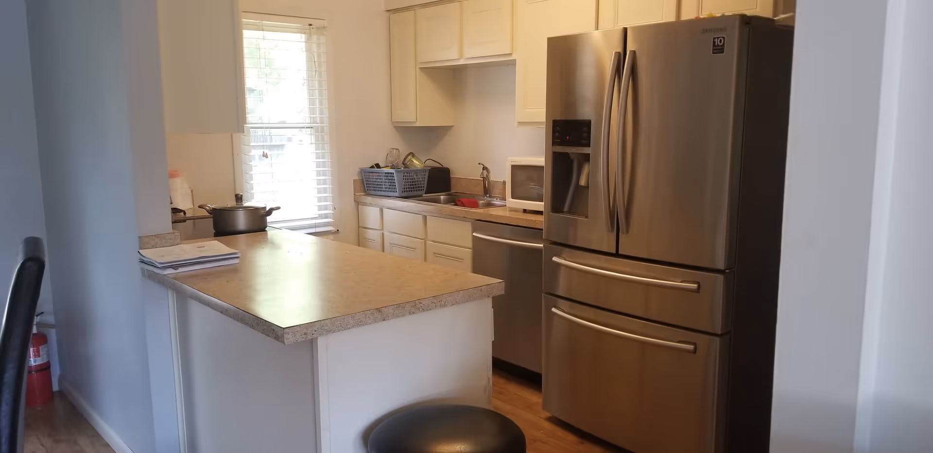 Small kitchen with a center island, stainless steel French-door refrigerator, sink, microwave and window.