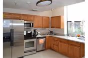 Well-lit kitchen with stainless steel refrigerator, oven, microwave and dishwasher, wooden cabinets and a large window.