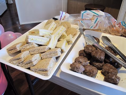 Trays of prepared sandwiches and sausage patties on a table in a dining area.
