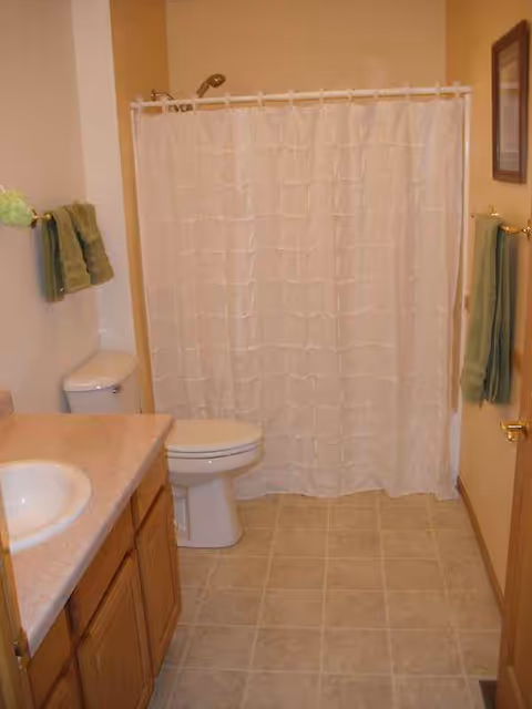 Bathroom with sink, toilet, and shower curtain in a senior living facility.