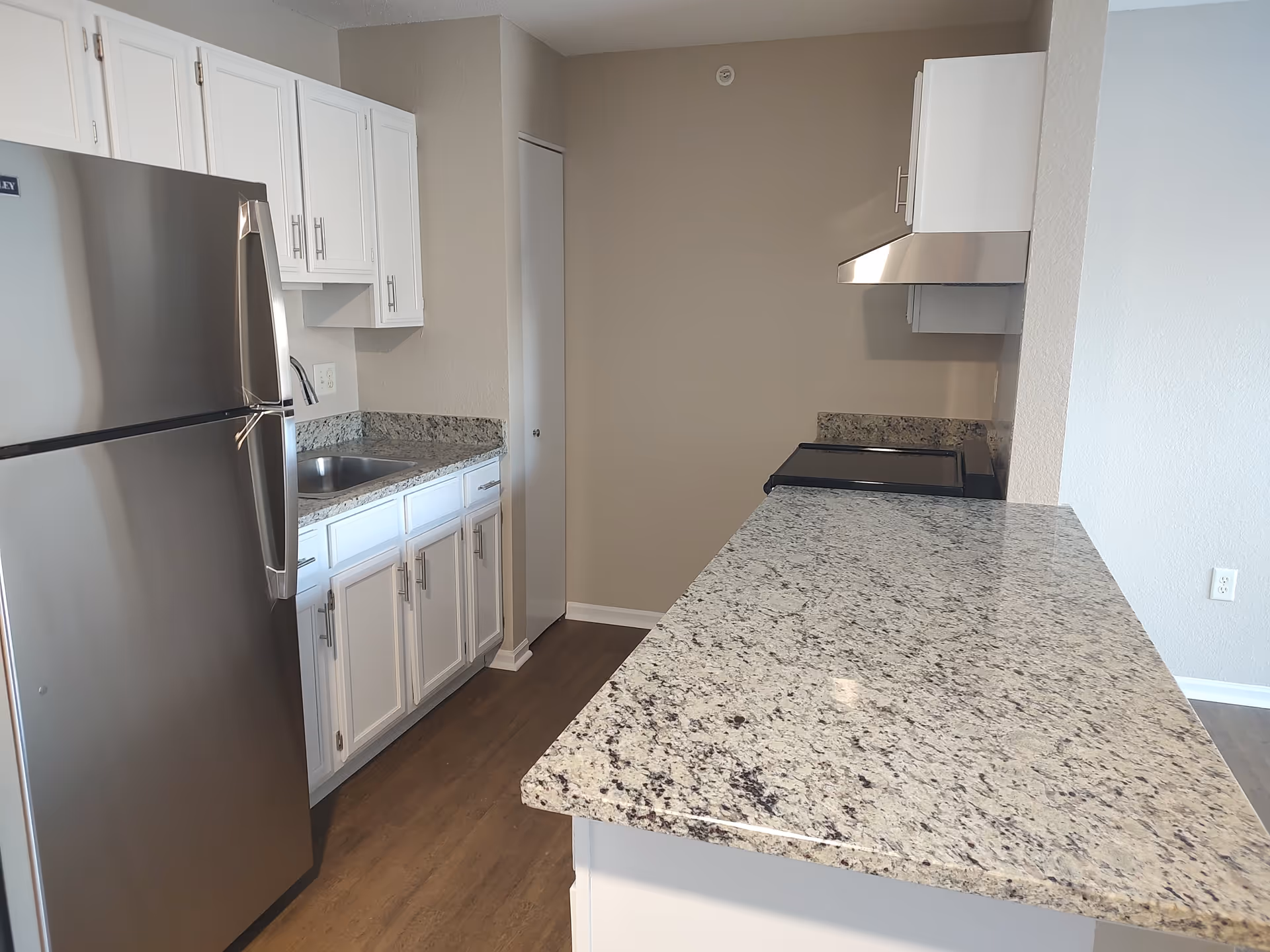 Modern kitchen with granite countertops, stainless steel refrigerator and stove, white cabinets, and wood-look flooring.
