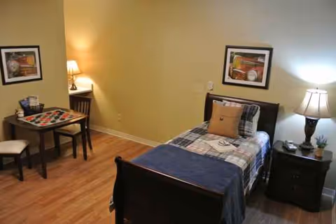 A single bedroom in a senior living room features a bed, nightstands, lamps, and framed art.