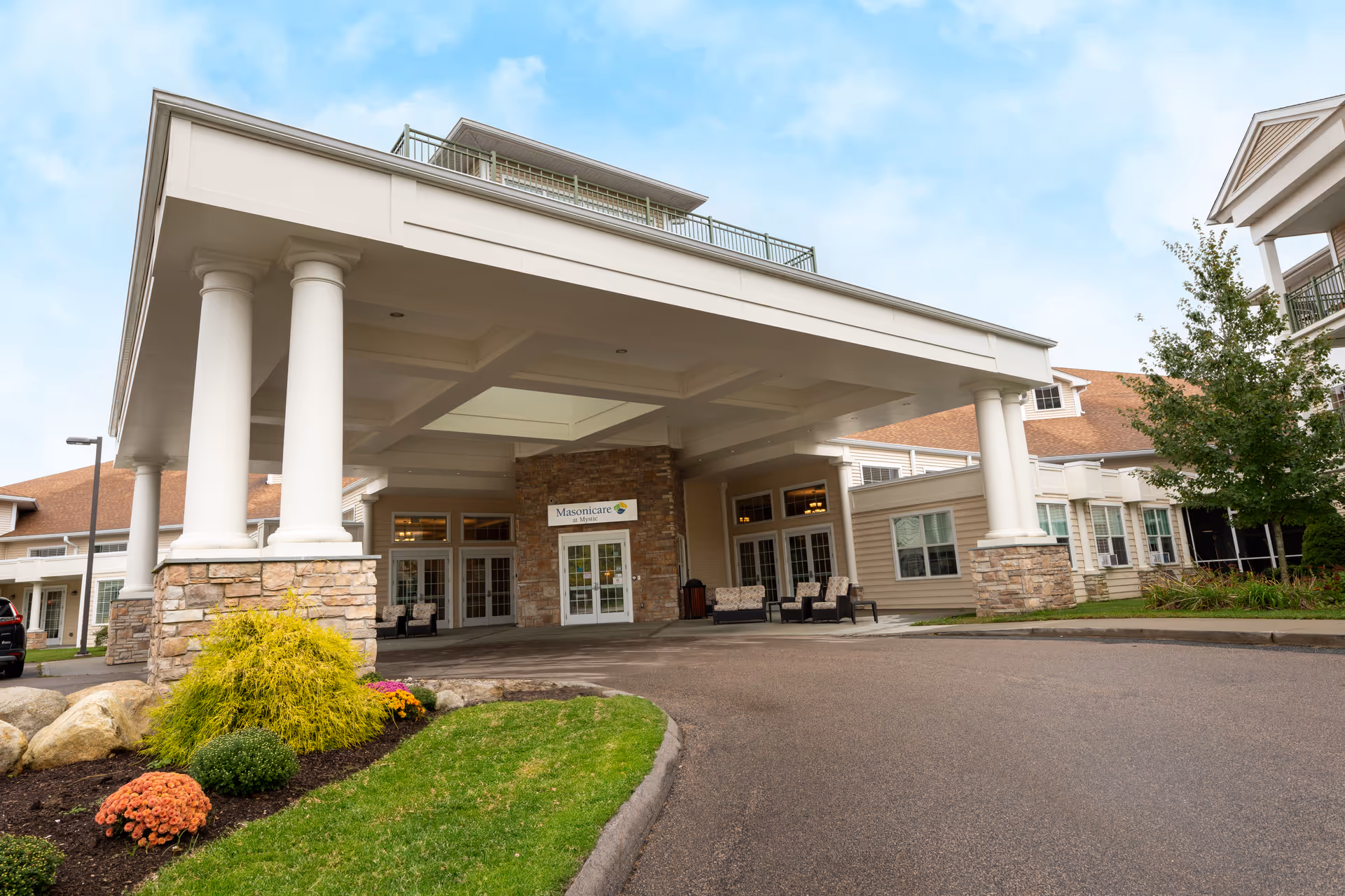 Covered entrance with tall white columns and a sign reading "Masonicare" at the front of a senior living facility.