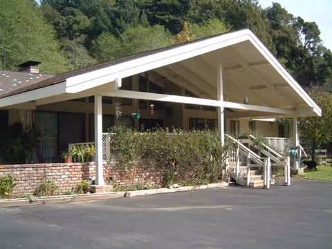Senior living facility with a white gabled roof, front porch, and surrounding shrubs.