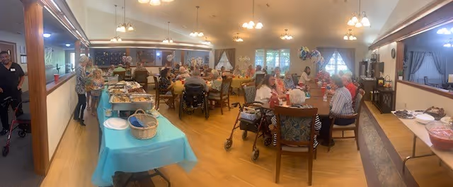 Panoramic interior of a communal dining room with seniors seated at multiple tables, buffet stations, and staff.