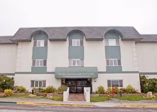 Exterior view of a beige three-story senior living facility with a central entrance.