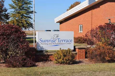 Sunrise Terrace sign in front of a brick building with landscaped shrubs.