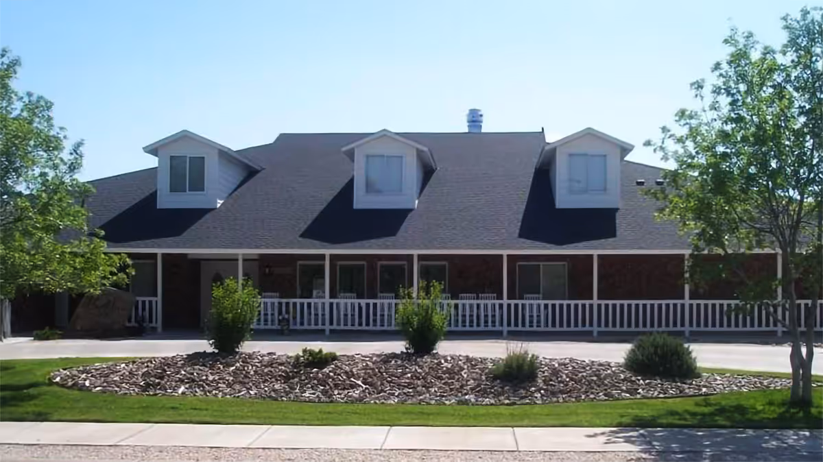 Front exterior of a single-story residential building with three dormer windows, a covered porch with white railing, and a landscaped rock bed and shrubs in front.