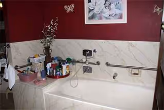 Bathroom with bathtub, wall-mounted grab bars, and toiletries on a tray under a maroon wall.