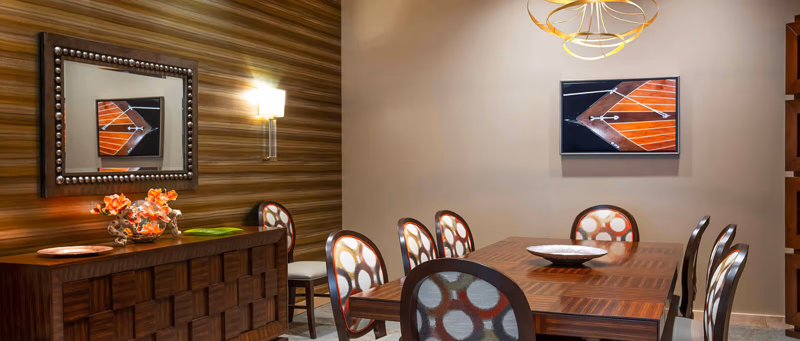 Modern dining room with a wooden table surrounded by patterned chairs, a sideboard with decorative items, a mirror and wall art.