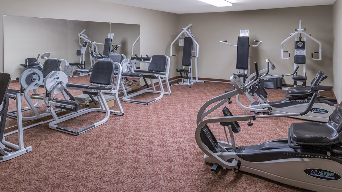 Carpeted exercise room with multiple recumbent cardio machines and strength equipment facing a mirrored wall.