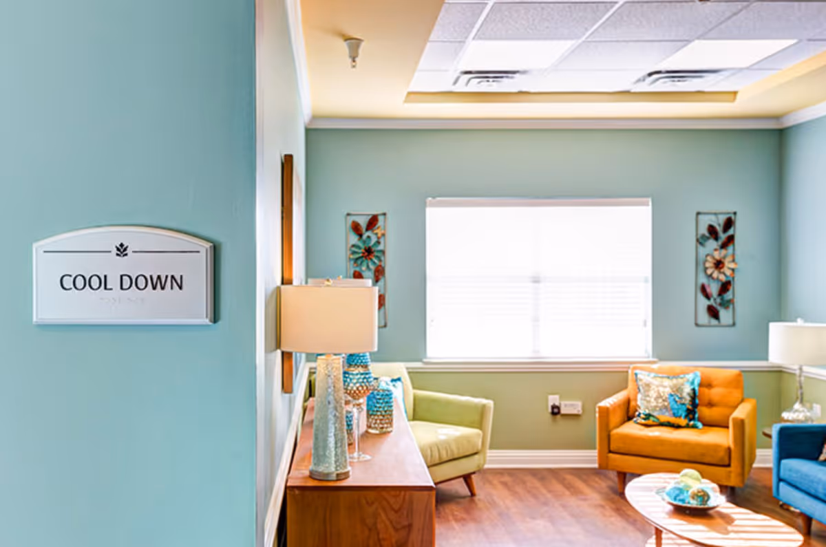 Sunlit common room with colorful armchairs, side tables and lamps and a wall sign reading "COOL DOWN".