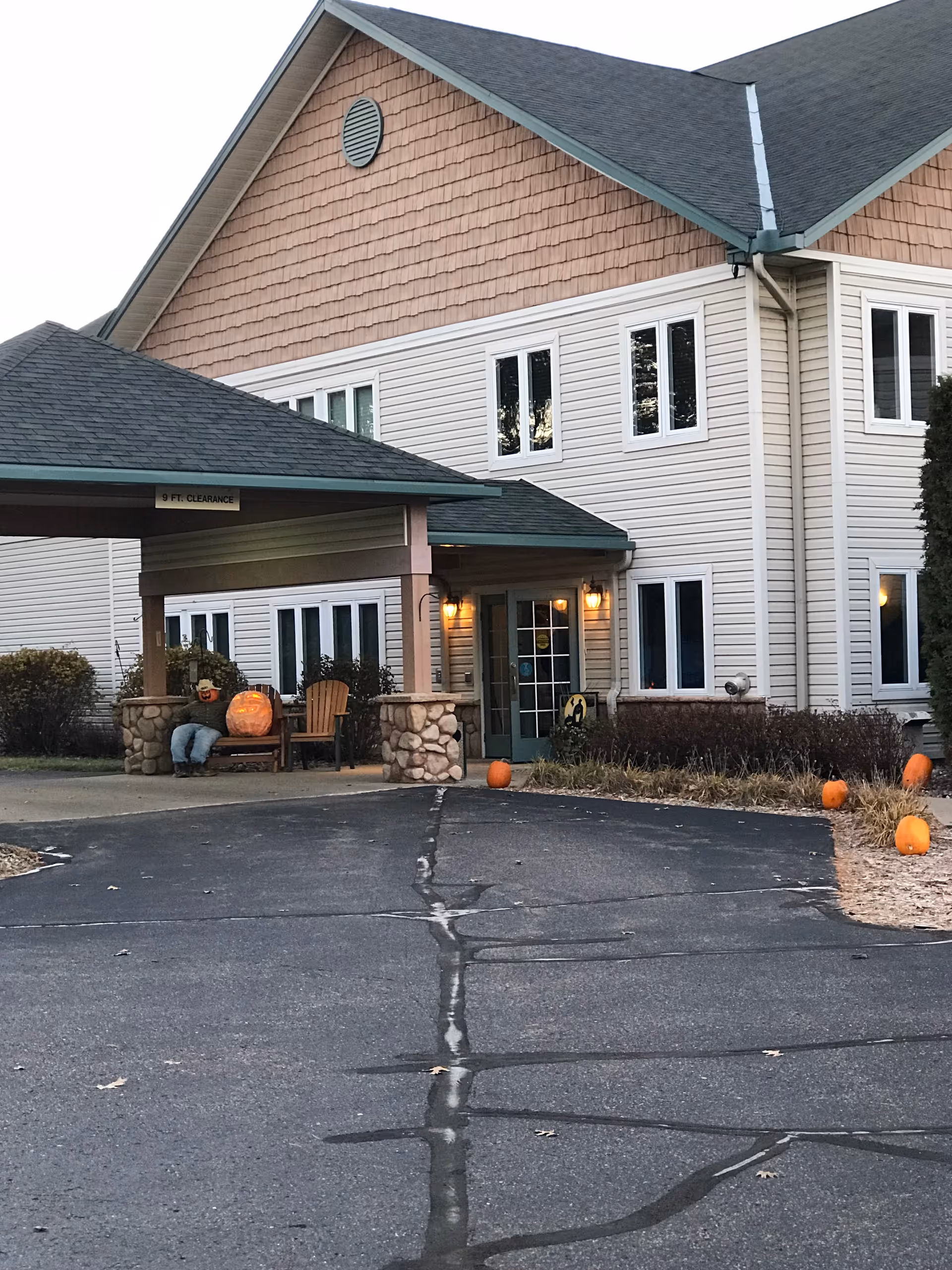 Entrance of a two-story assisted living building with a covered portico, pumpkins and fall decorations at the doorway.