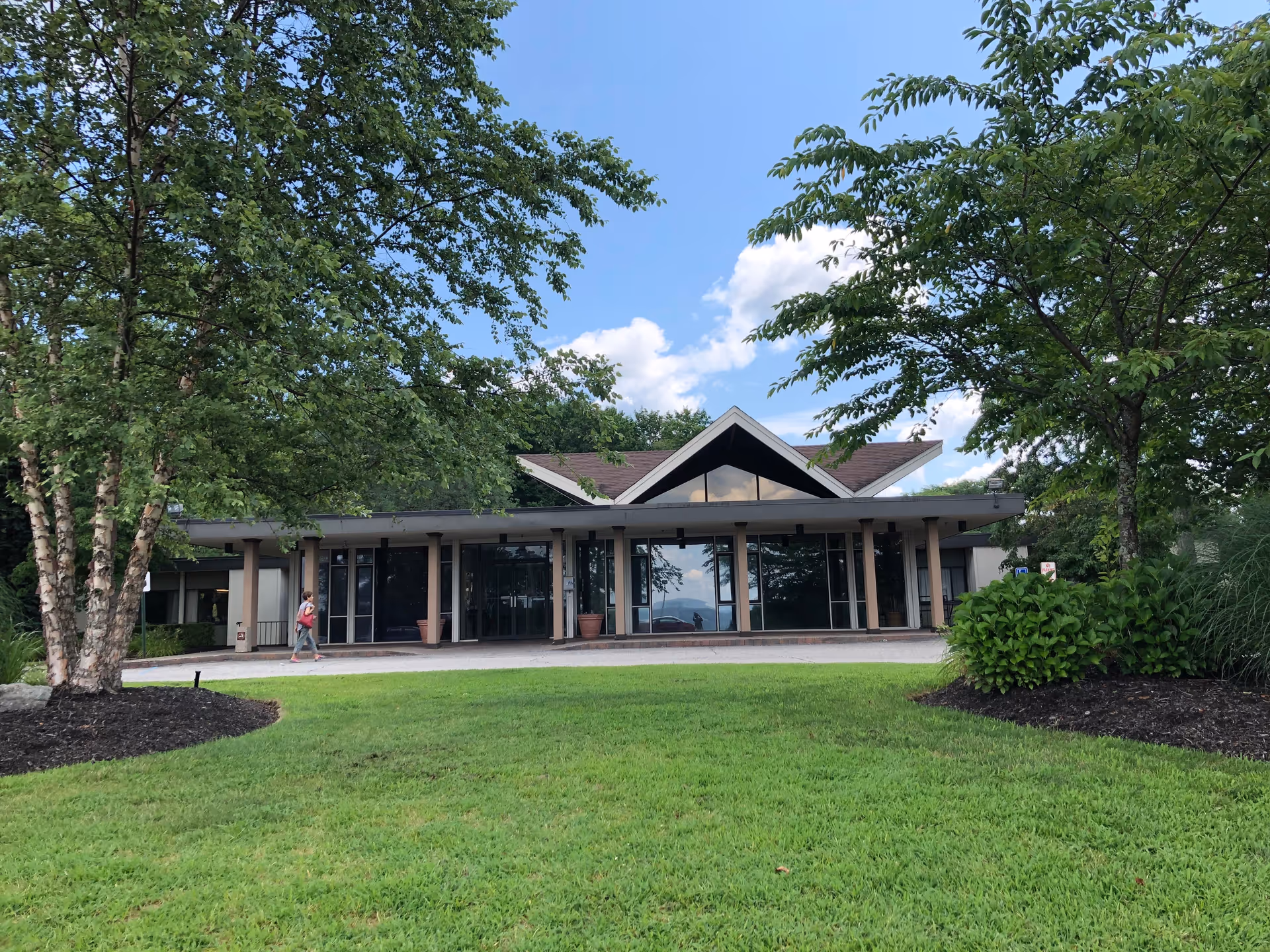 Front exterior view of Cedar Manor Nursing & Rehabilitation Center building with a green lawn and trees in the foreground under a blue sky with some clouds.