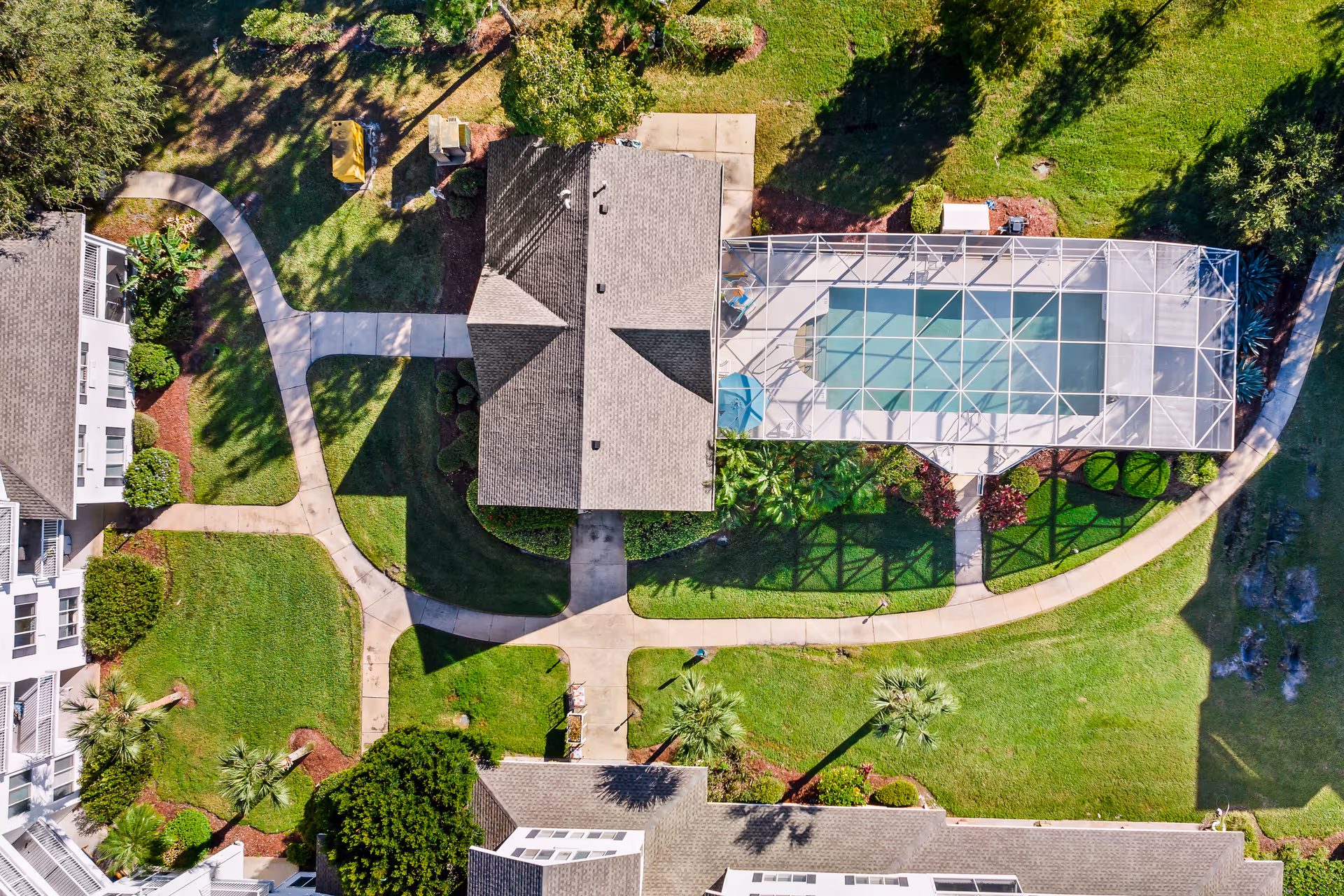 Aerial view of a senior living community showing buildings, walkways, green lawns, and a screened-in swimming pool area surrounded by landscaped gardens.