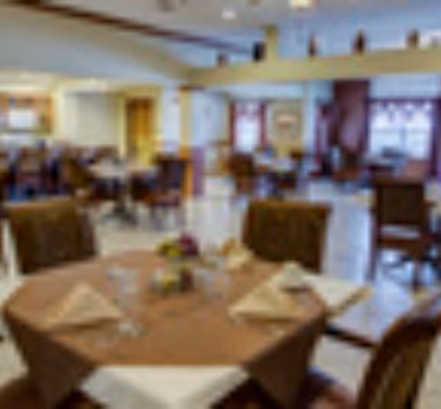 Dining room with round tables set with napkins and chairs in a senior living facility.