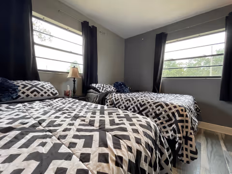 Three twin beds with geometric bedding in a shared bedroom with large windows.