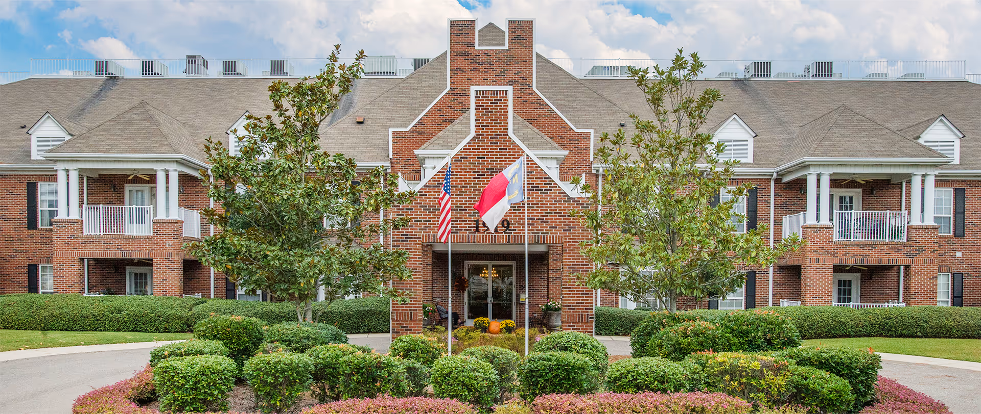 Exterior of The Carolina Highlands at Village Green, a brick senior living building with landscaped grounds.