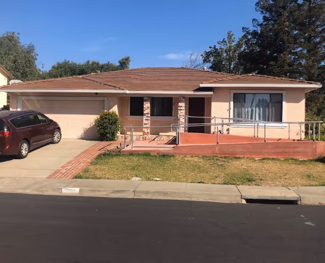 Single-story pink stucco house with an attached garage, front wheelchair ramp, and a red minivan parked in the driveway.