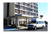 Exterior view of St Mark's Towers building entrance with a covered drop-off area and a white passenger van parked in front. The building is multi-story with numerous windows and a clear blue sky in the background.