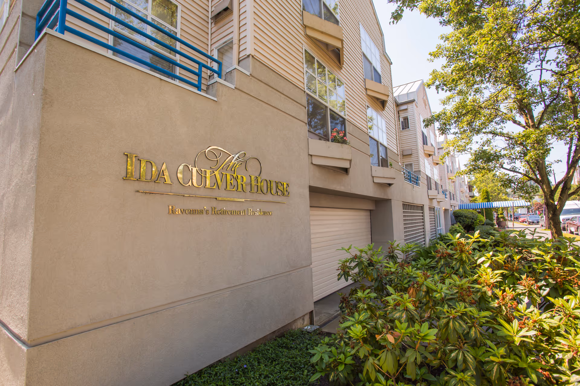 Exterior front of the Ida Culver House building with gold signage, windows and balconies above landscaped shrubs.