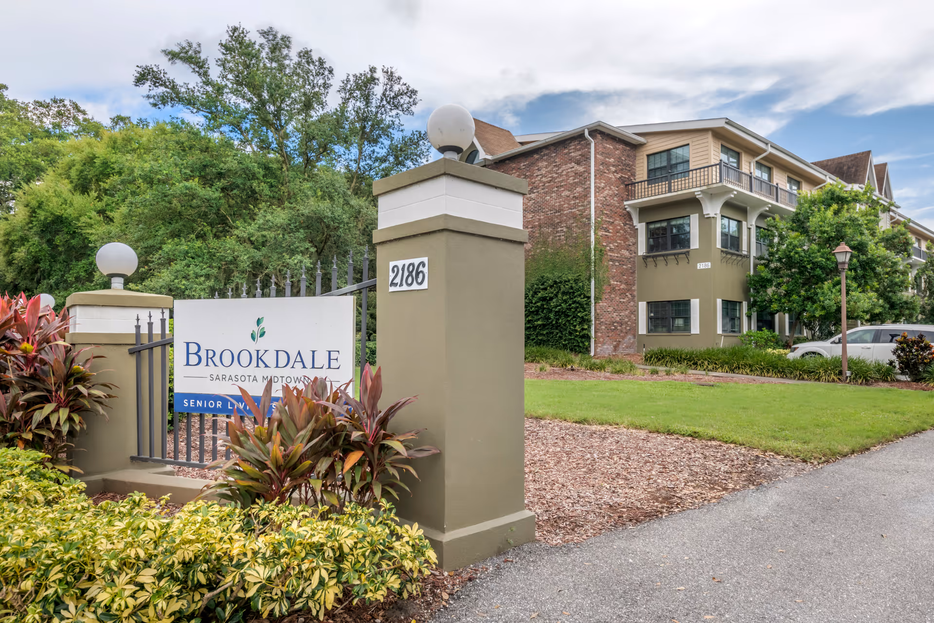Entrance sign and landscaped front of Brookdale Sarasota Midtown senior living building with pillars and a three-story brick-and-stucco facade.