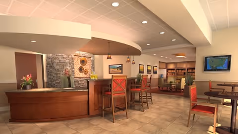 Reception area of Discovery Village Stone Oak featuring a curved wooden front desk with a staff member standing behind it, stone accent wall with decorative art, pendant lights hanging from the ceiling, and seating area with tables and chairs in the background.