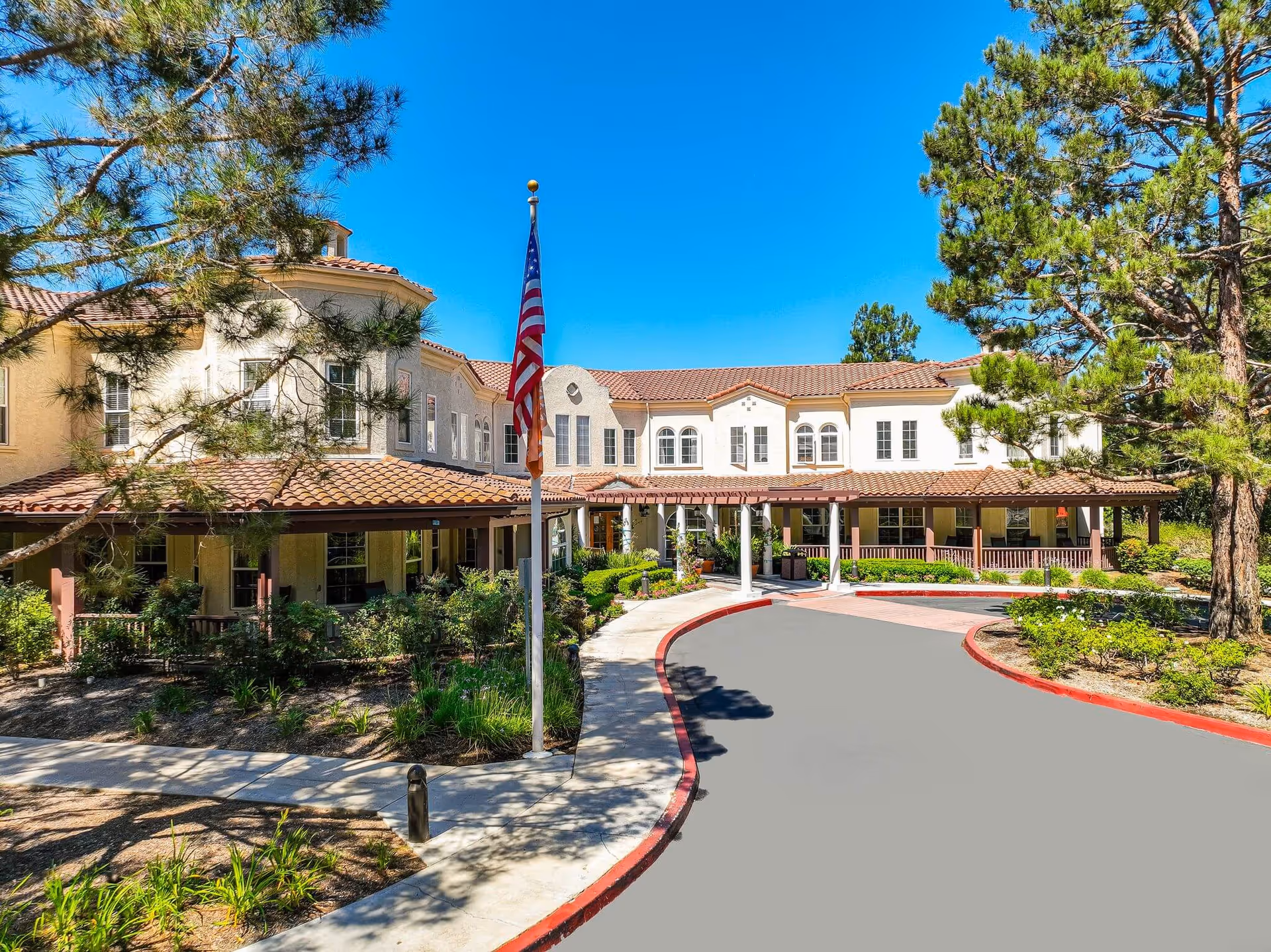 Exterior view of Sunrise of Mission Viejo, a senior living facility with driveway, flag, and trees.
