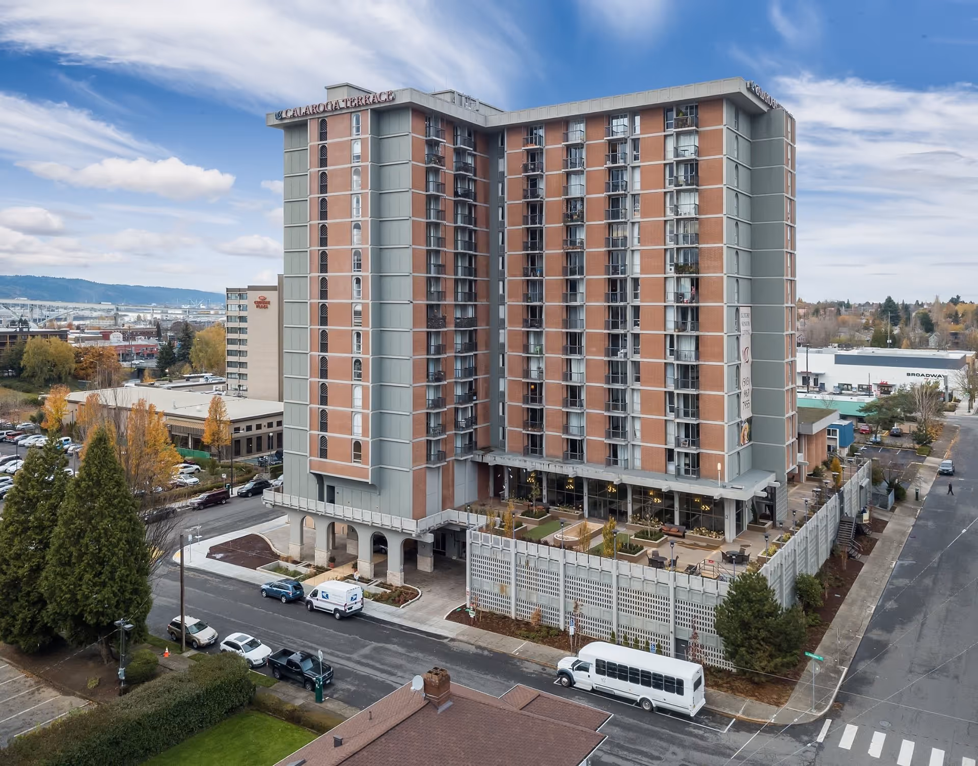 Exterior view of a tall multi-story building named Calaroga Terrace, surrounded by streets, parked vehicles, trees, and other buildings under a partly cloudy sky.