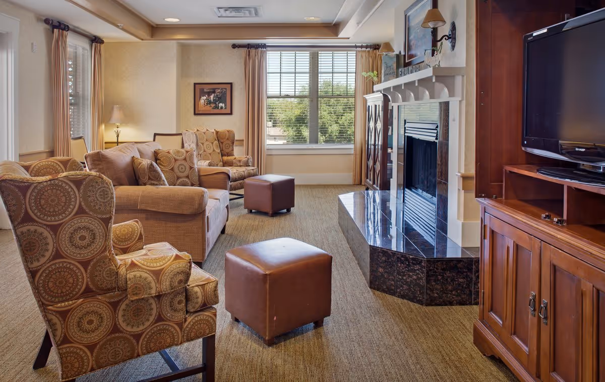 Cozy living room with patterned armchairs, sofas, ottomans, a fireplace, and a TV cabinet by a sunlit window.