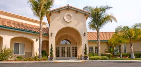 Spanish-style senior living facility entrance with arches, palm trees, and a tiled roof.