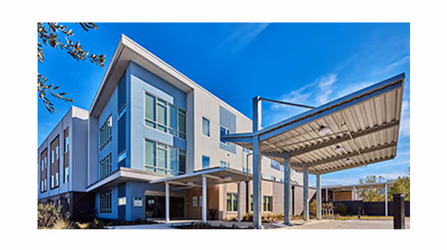 Exterior view of a modern three-story building with large windows and a covered entrance area under a clear blue sky.