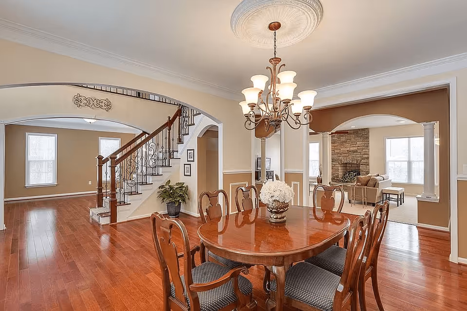 Open dining room with a wooden table and chairs under a chandelier, hardwood floors, and a view of a staircase and adjoining living room.