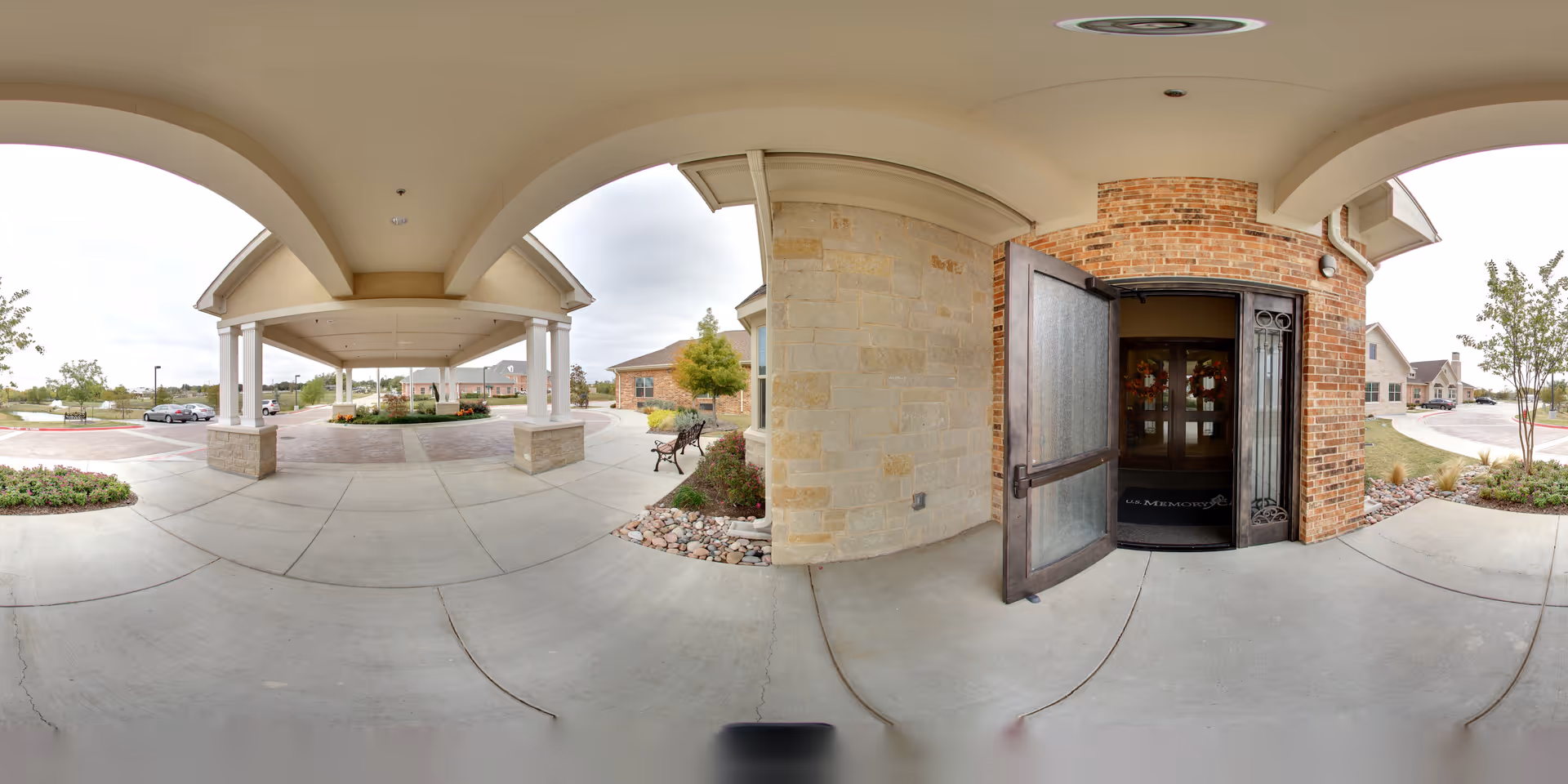 Covered porte-cochere and main entrance of Ellery Arbor with an open decorative door, brick and stone facade, benches, and a circular drive-up area.