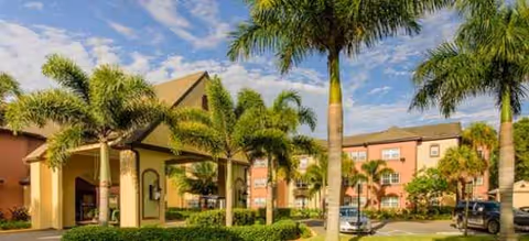 Brookdale College Parkway exterior with palm trees, beige buildings, and parked cars in the parking lot.