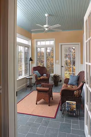 Sunlit living room in a senior living facility with chairs, a rug, and a ceiling fan.