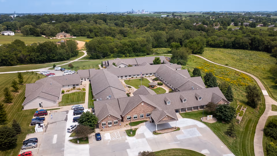 Aerial view of a single-story assisted living facility with a central courtyard, parking lot, and surrounding lawns and walking paths.