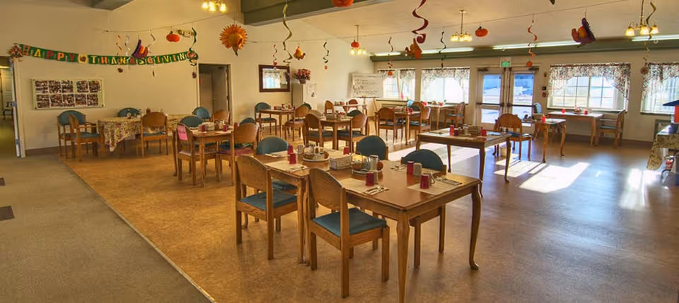 Large dining room decorated for a holiday with multiple wooden tables and chairs set with place settings.
