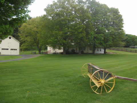 A green lawn surrounds a white building with trees and a wagon wheel upfront.