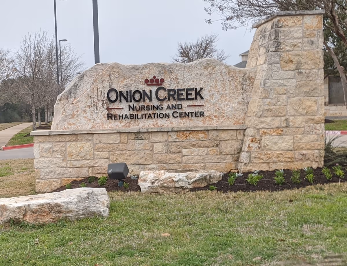 Stone sign at Onion Creek Nursing and Rehabilitation Center with landscaping and trees in the background.
